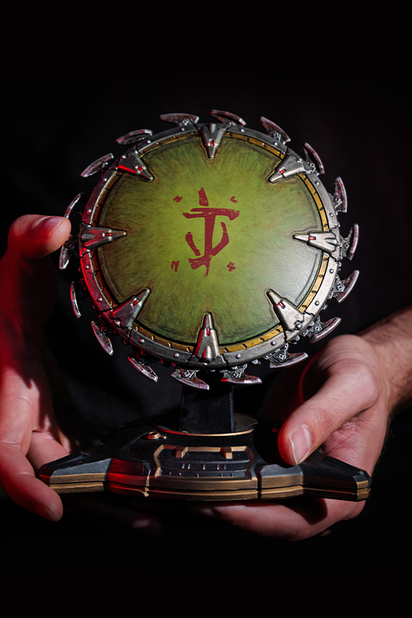 Hand holding a circular trophy with green center and red symbol against a dark background