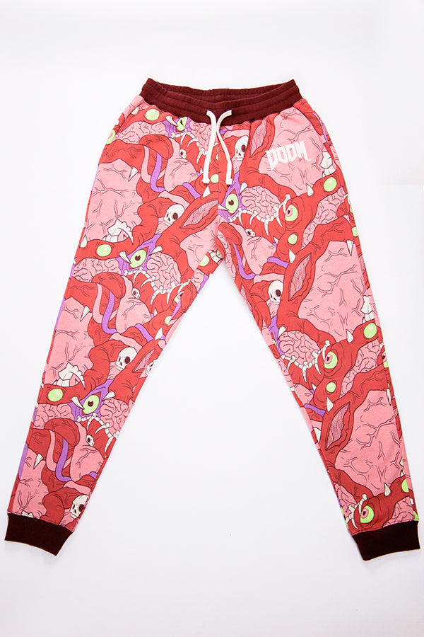Overhead shot of the DOOM Meat Sweats, a pair of comfy unisex sweatpants with a tapered jogger fit. They feature an all-over print of scrambled demon meat and bones (eyes, teeth, brains, intestines, skulls, and muscles), ribbed burgundy cuffs and waistband, and a white DOOM logo appliqué on the wearer’s left hip.
